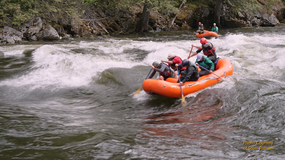 Group white water rafting in turbulent river rapids with orange inflatable boat and paddles