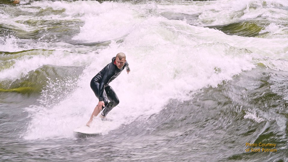 Surfer in black wetsuit riding a wave with white foam crest
